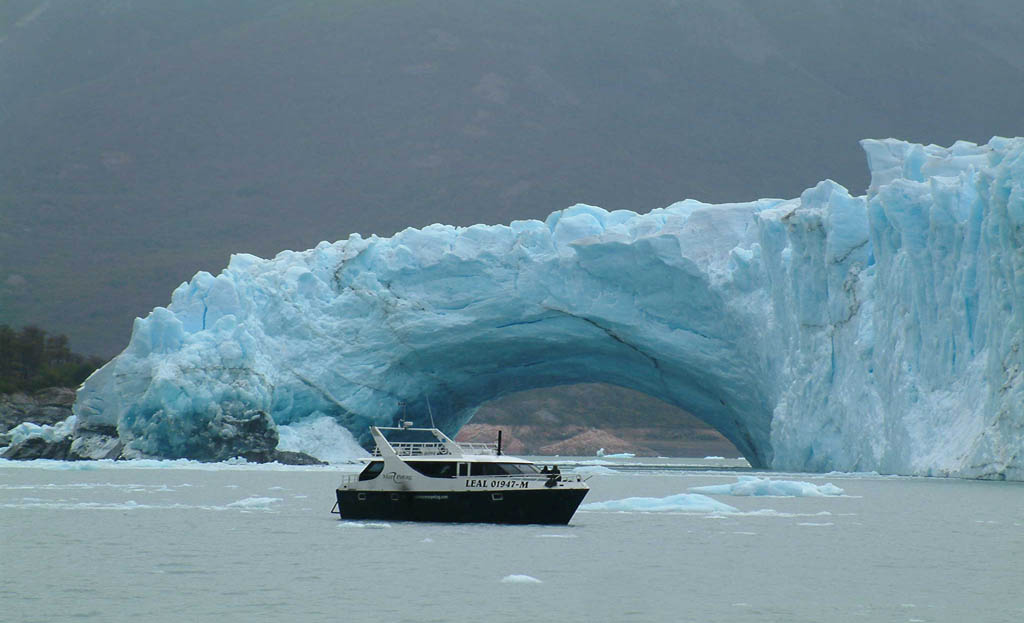 Petit bateau naviguant devant une arche naturelle de glace du glacier Perito Moreno, El Calafate