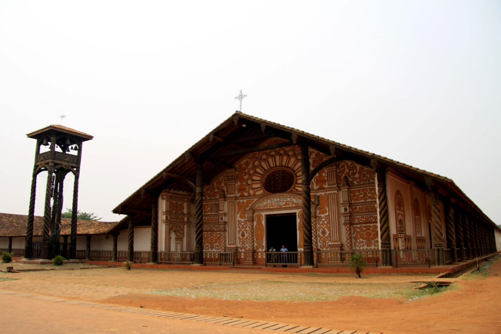 Église-mission de Concepción en Bolivie, façade peinte à motifs, colonnes torsadées et clocher en bois séparé