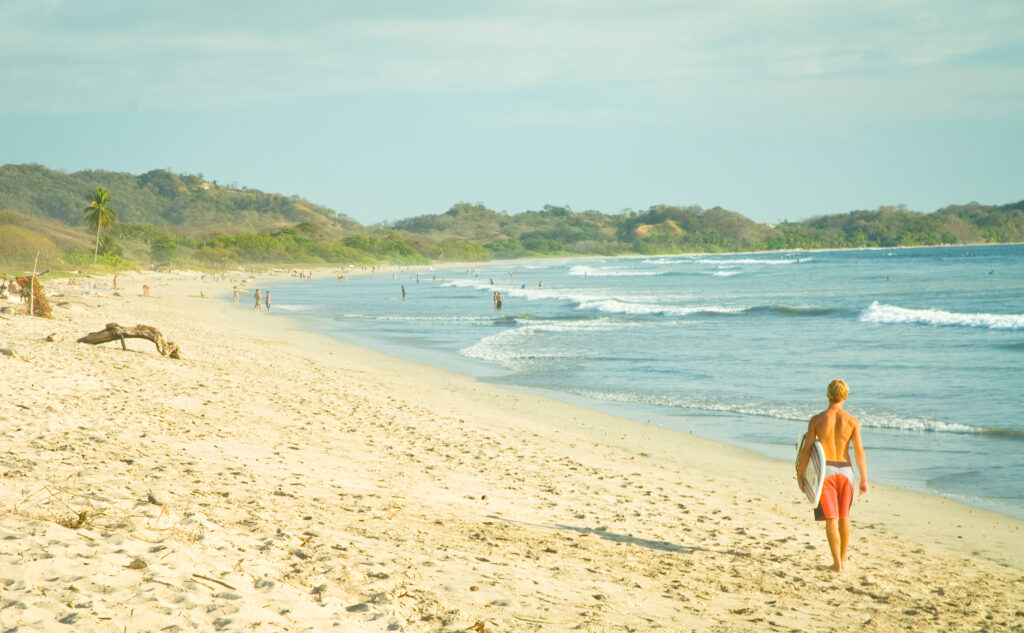 Surfeur marchant vers l'océan sur une plage de sable, péninsule de Nicoya, Costa Rica