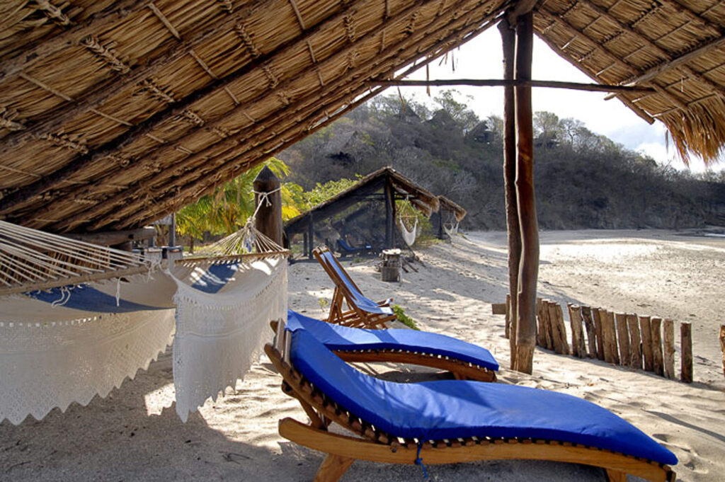 Transats bleus et hamacs blancs sous un toit de chaume, plage de sable au Nicaragua