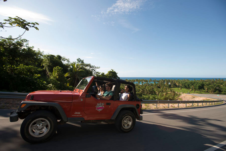 Jeep rouge décapotable avec touristes roulant sur route côtière asphaltée à Samana, République Dominicaine