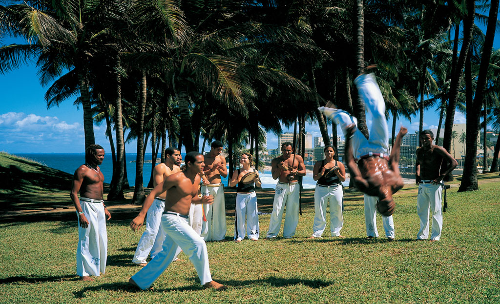 Groupe pratiquant la capoeira sous les palmiers face à l'océan à Salvador de Bahia