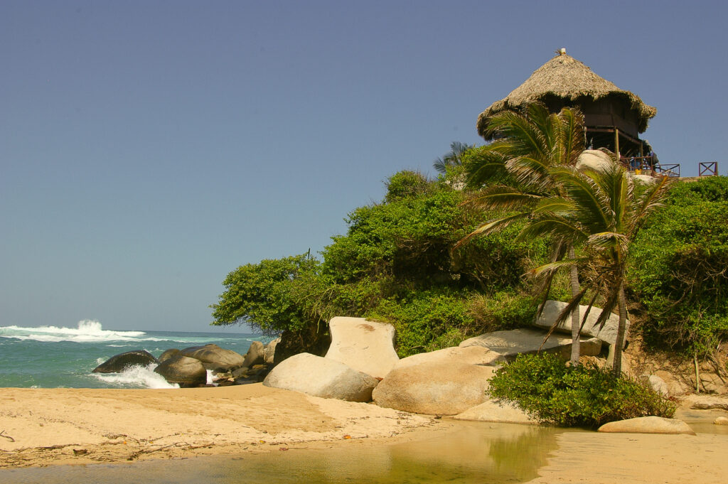 Plage de sable avec rochers, palmiers et hutte au toit de chaume au Parc Tayrona, Colombie