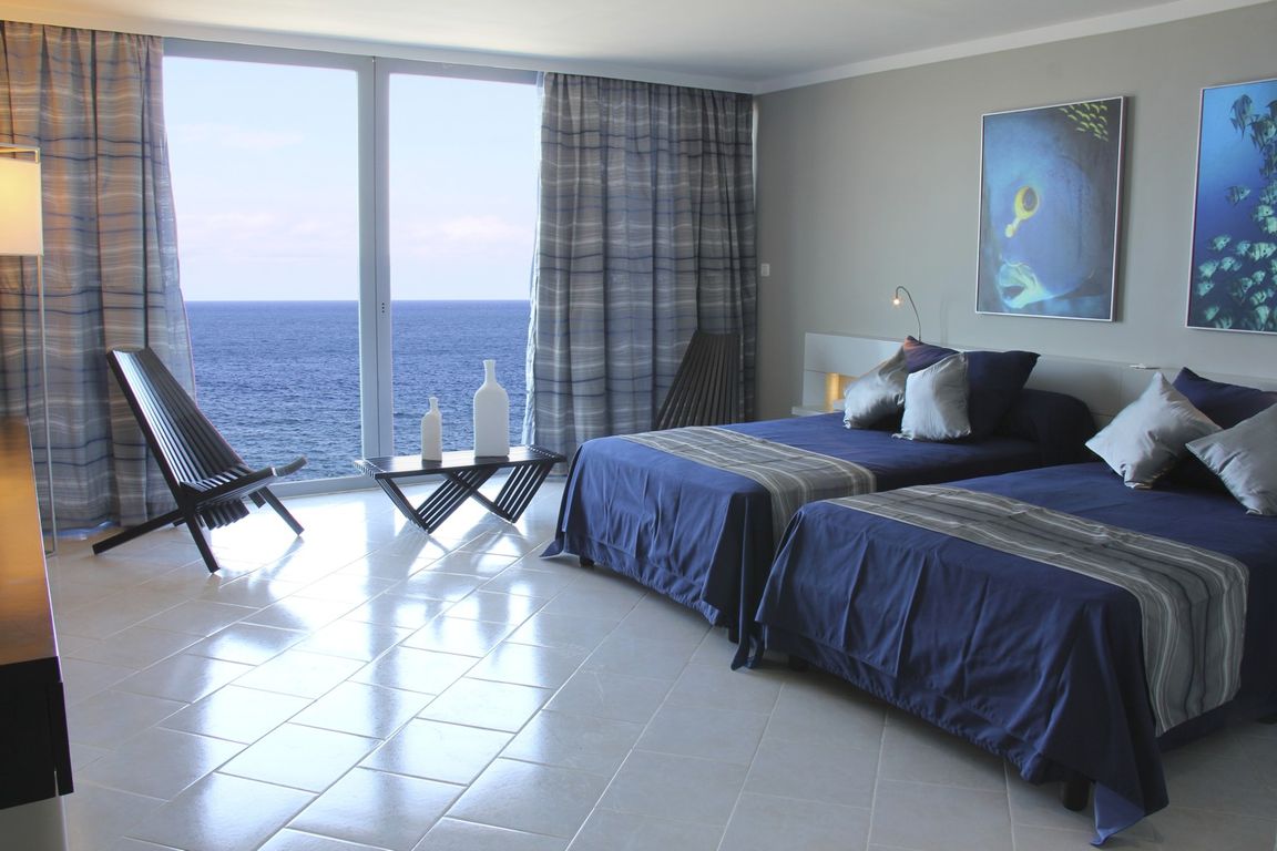 Chambre d'hôtel aux tons bleus avec deux lits et vue panoramique sur l'océan