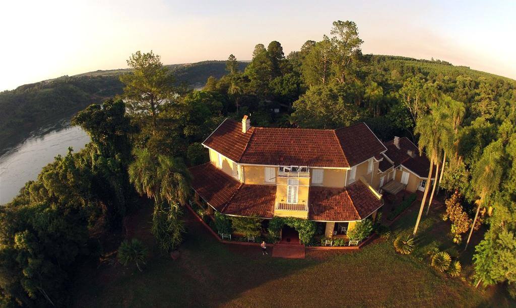 Vue aérienne d'une maison à toit rouge entourée d'arbres près d'une rivière en Argentine