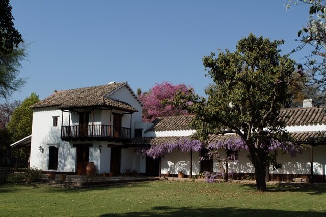 Hacienda coloniale blanche avec balcon en bois et arbres fleuris violets, région de Salta, Argentine