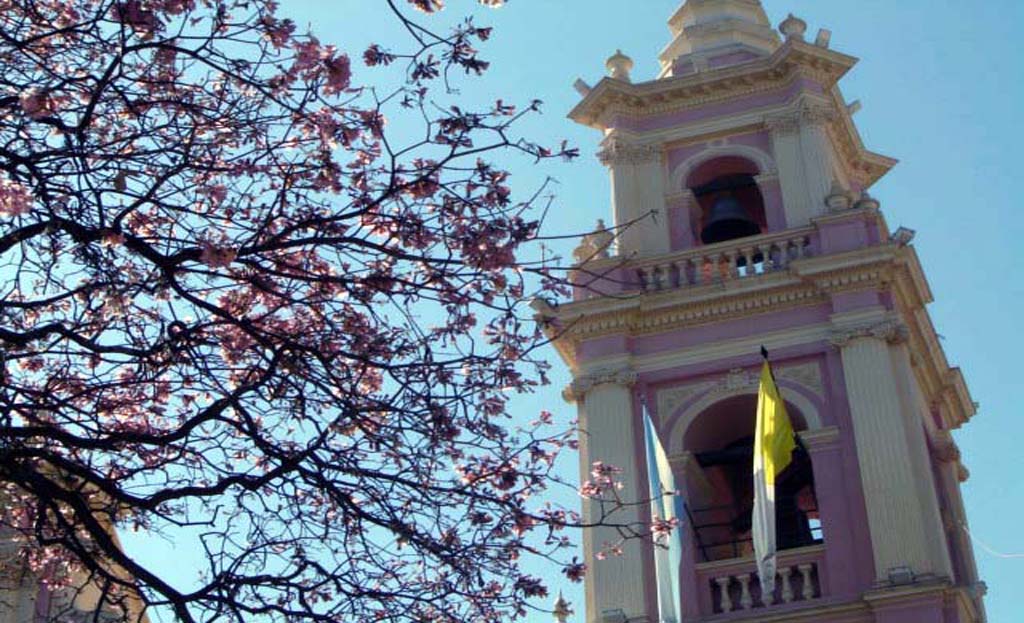 Clocher rose orné d'une église à Salta, avec cloche, drapeaux et arbre en fleurs