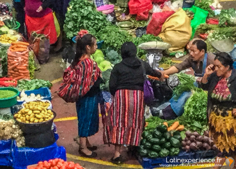 Marché de légumes au Guatemala avec vendeurs et acheteurs en tenues traditionnelles colorées