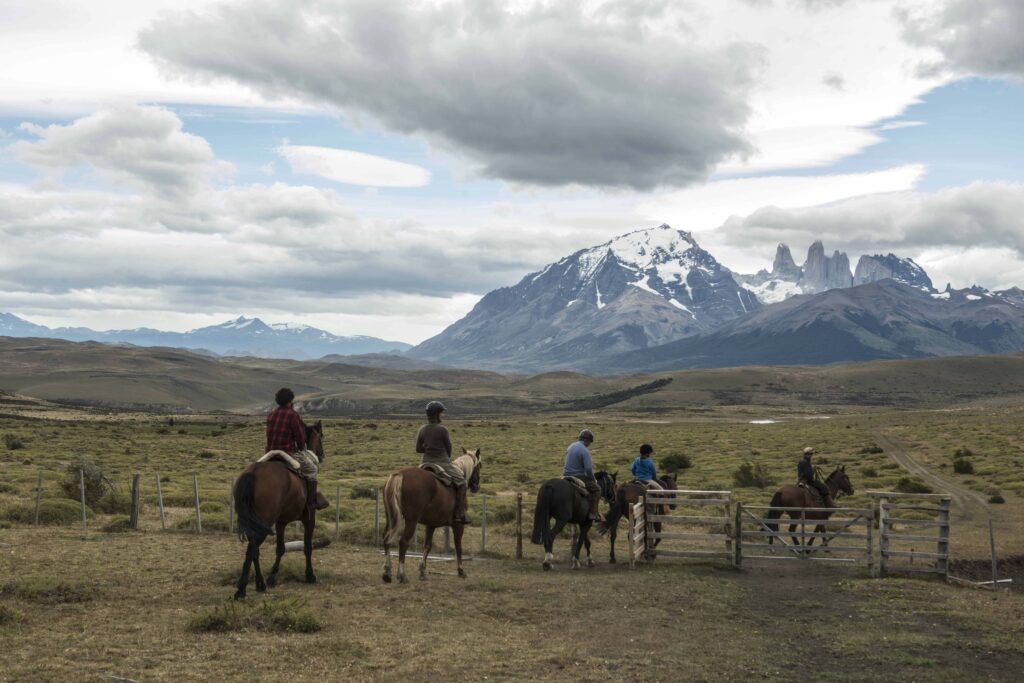 Cavaliers à cheval traversant un enclos face aux tours de granite de Torres del Paine, Patagonie chilienne