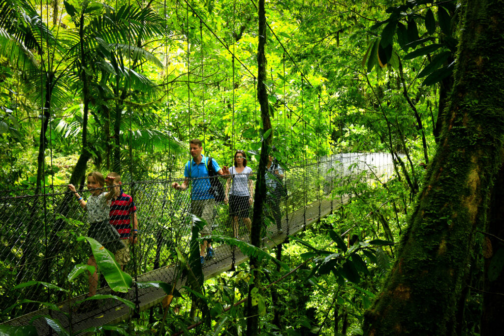 Famille traversant un pont suspendu métallique dans la forêt tropicale près du volcan Arenal, Costa Rica