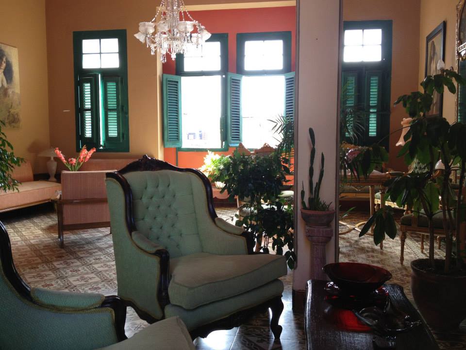 Salon cubain traditionnel avec fauteuils anciens, volets verts et lustre en cristal