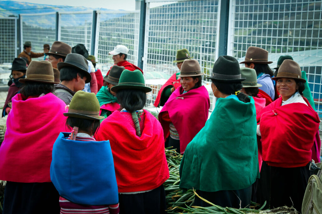 Groupe de femmes équatoriennes en châles colorés et chapeaux devant un marché de légumes en plein air