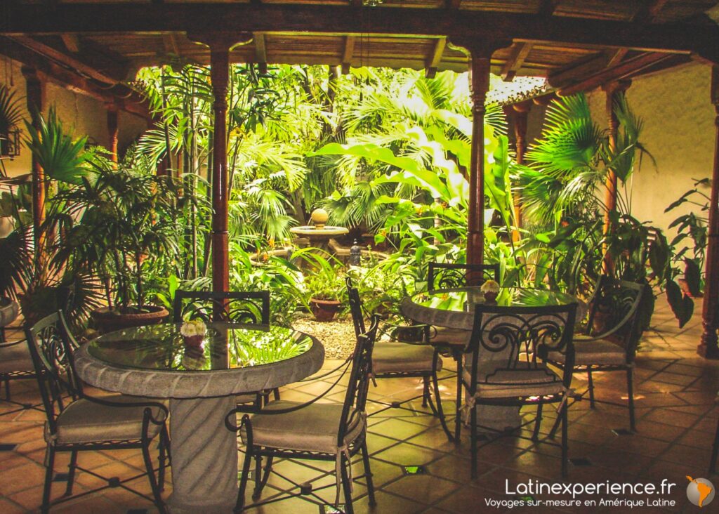 Patio couvert d'un hôtel avec tables rondes, chaises en fer forgé et fontaine entourée de plantes tropicales, Nicaragua