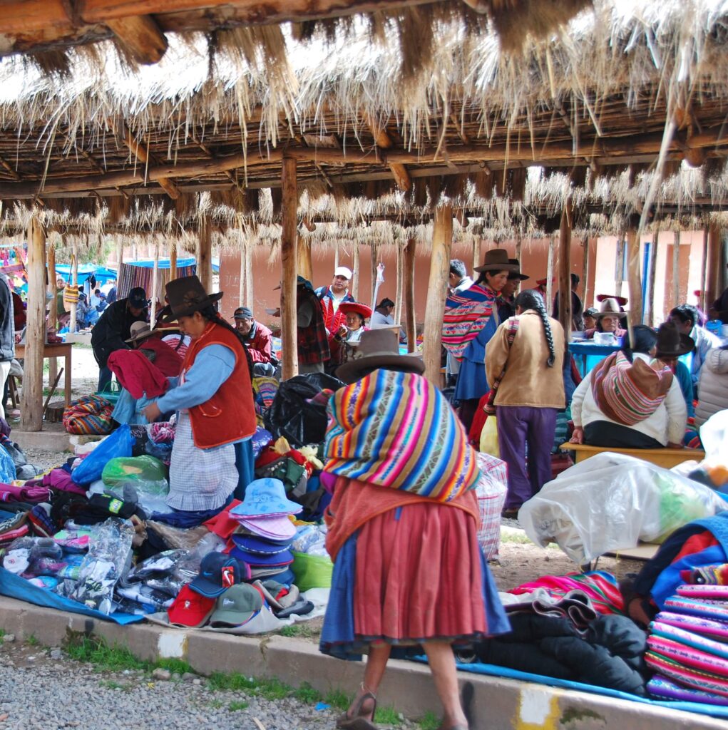Marché péruvien couvert de chaume avec vendeurs en habits traditionnels et articles textiles étalés au sol