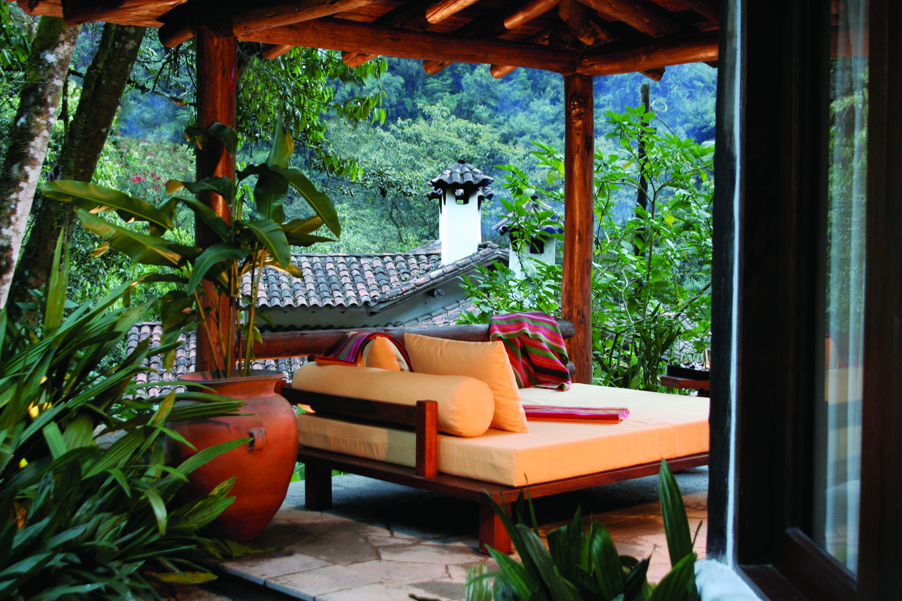 Terrasse en bois d'un lodge péruvien avec banquette orange face à la forêt tropicale