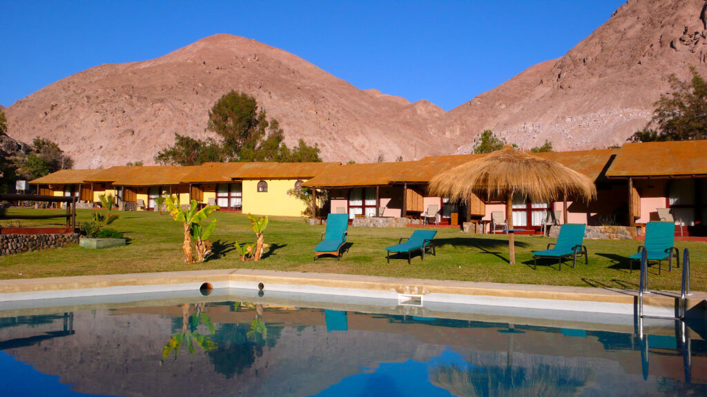 Piscine et bungalows d'un hôtel oasis au Chili, entourés de montagnes désertiques arides