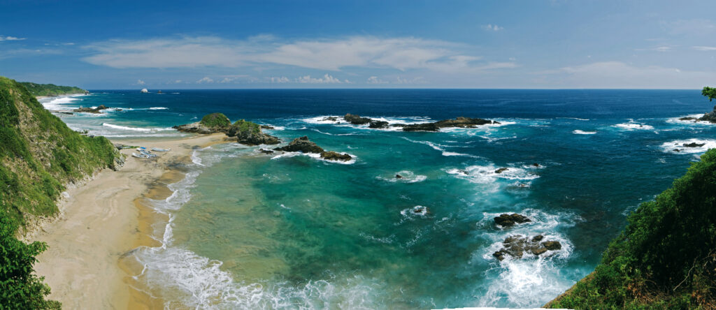Vue panoramique d'une plage de sable avec bateaux échoués, collines verdoyantes et rochers dans l'océan Pacifique mexicain