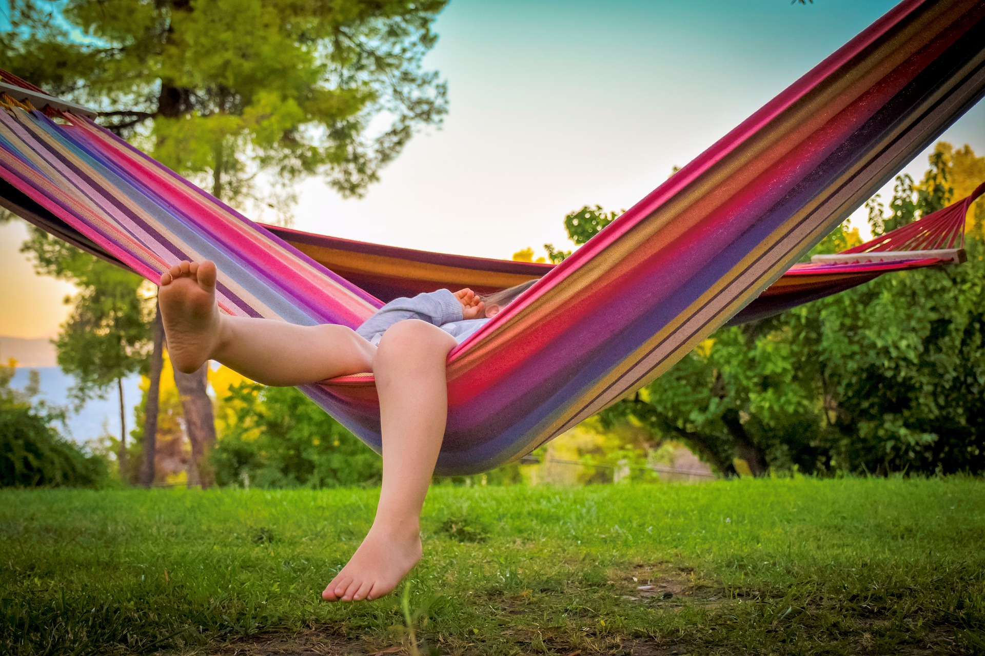 Enfant pieds nus allongé dans un hamac coloré au milieu d'arbres et d'herbe
