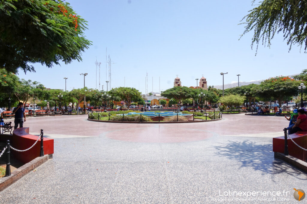 Place principale au Pérou avec fontaine circulaire, arbres fleuris et clochers d'église en arrière-plan