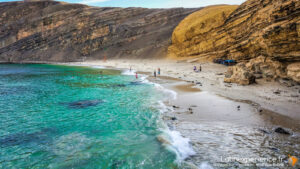 Plage de sable blanc bordée de falaises ocres et eau turquoise au Pérou