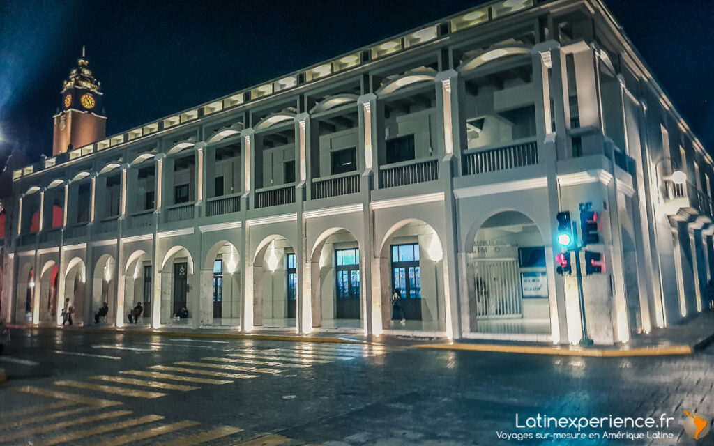 Bâtiment blanc à arcades illuminé la nuit avec tour de l'horloge à Mérida, Mexique