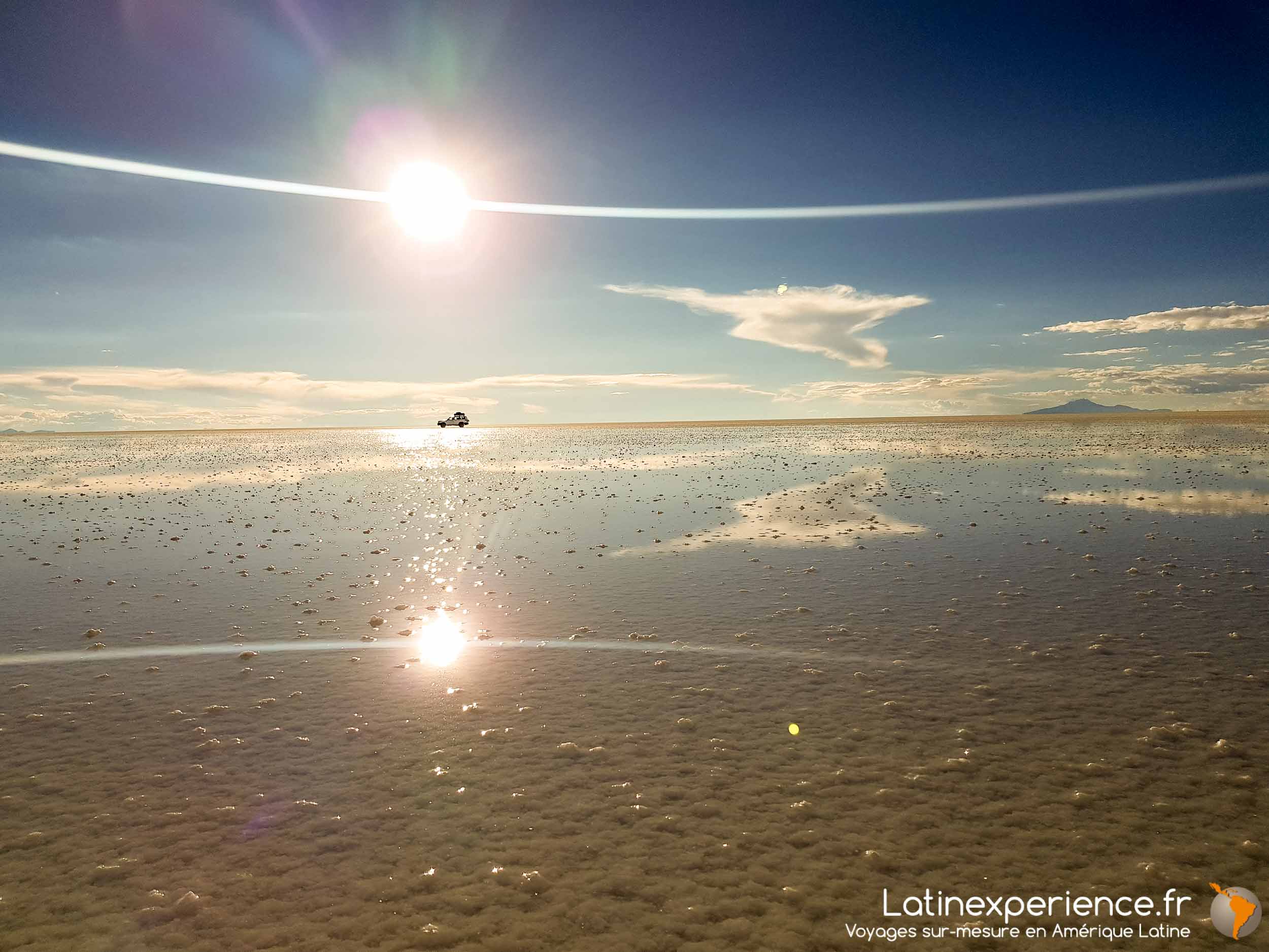 4x4 traversant un salar inondé reflétant le ciel et le soleil bolivien