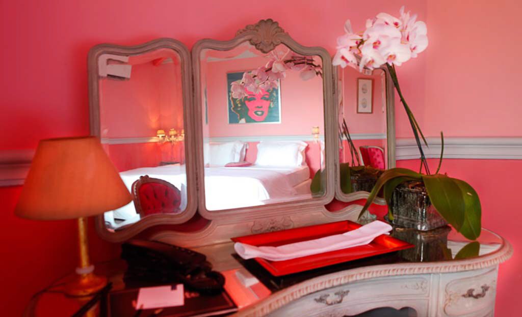 Coiffeuse rose avec miroir triptyque, orchidée et lit reflété dans une chambre d'hôtel