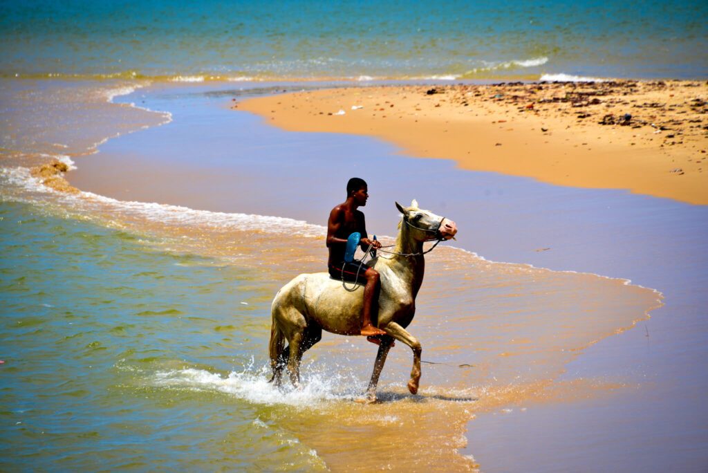 Homme à cheval traversant l'eau peu profonde sur la plage de Pontal do Maceio, Brésil