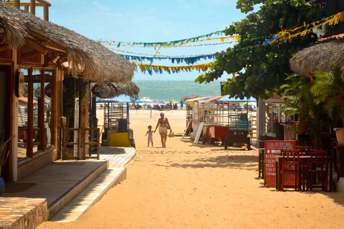 Rue de sable avec restaurants et cabanes de plage à Jericoacoara, femme et enfant marchant vers l'océan
