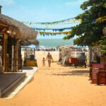 Rue de sable avec restaurants et cabanes de plage à Jericoacoara, femme et enfant marchant vers l'océan