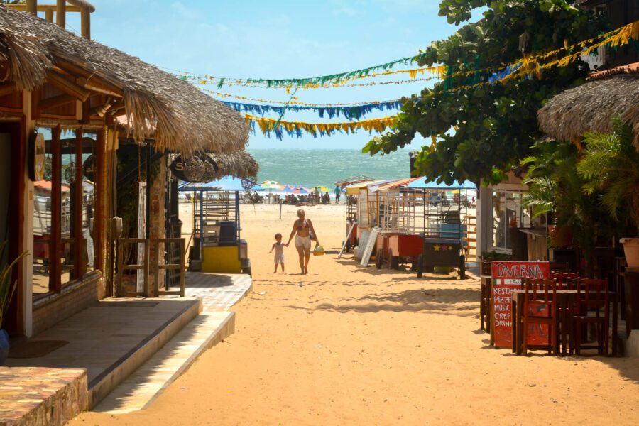 Rue de sable avec restaurants et cabanes de plage à Jericoacoara, femme et enfant marchant vers l'océan