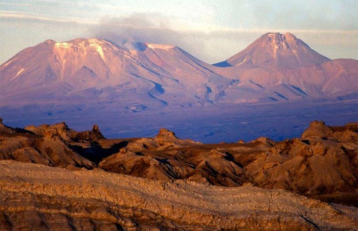 Volcans enneigés surplombant le désert et les formations rocheuses de San Pedro de Atacama, Chili