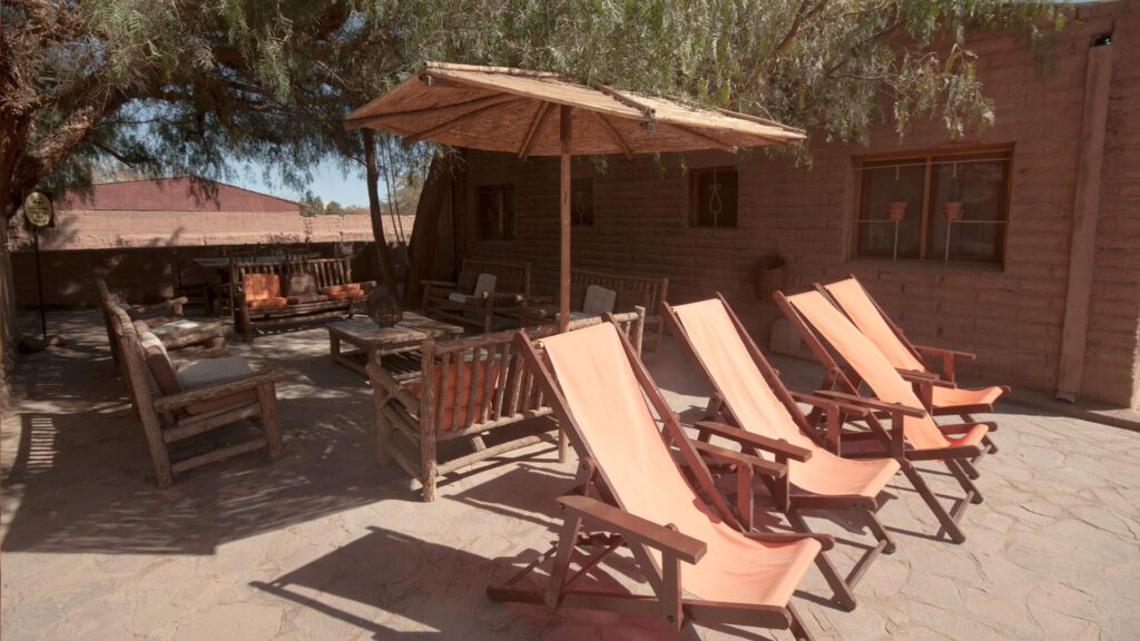 Terrasse ombragée avec transats orange et mobilier en bois dans un hôtel du désert d'Atacama