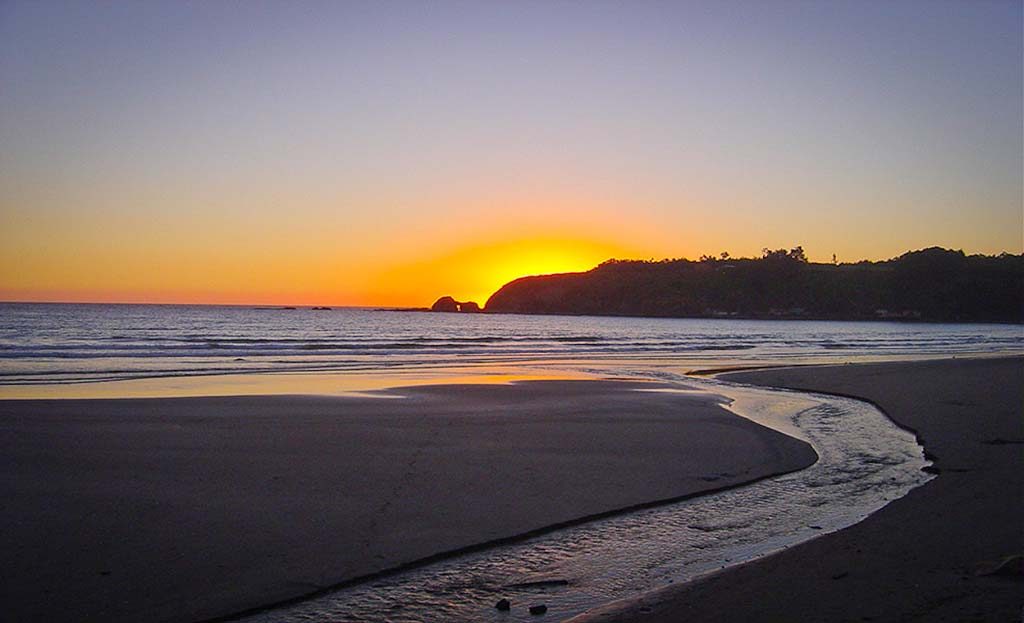 Coucher de soleil orangé sur une plage de sable avec colline en silhouette, Chili