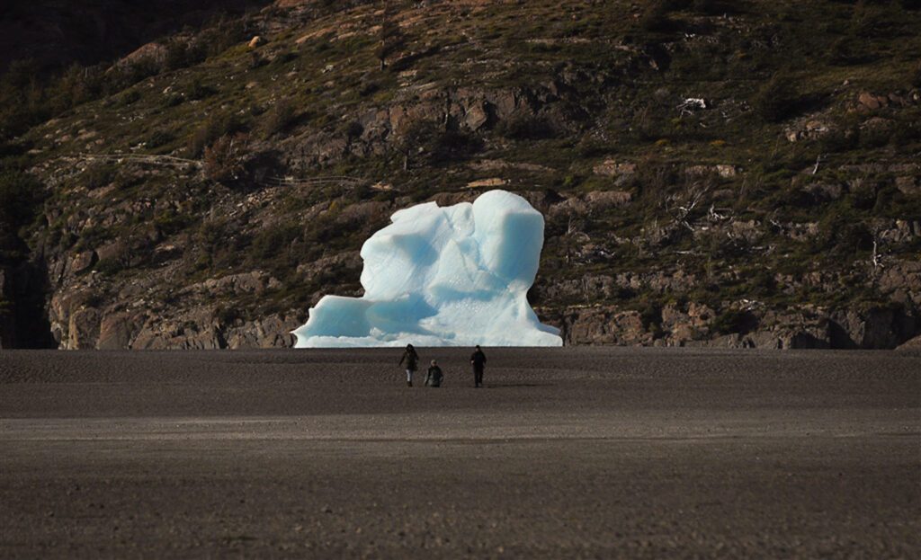 Trois randonneurs marchent sur une plage face à un iceberg échoué en Patagonie chilienne