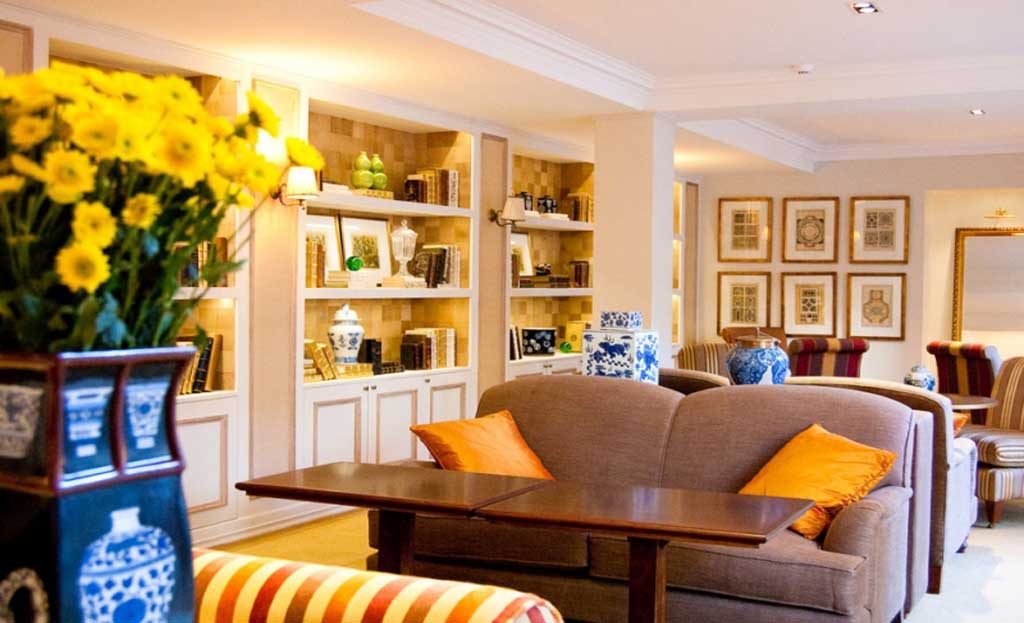 Salon d'hôtel avec canapés, fleurs jaunes, étagères et vases décoratifs bleu et blanc