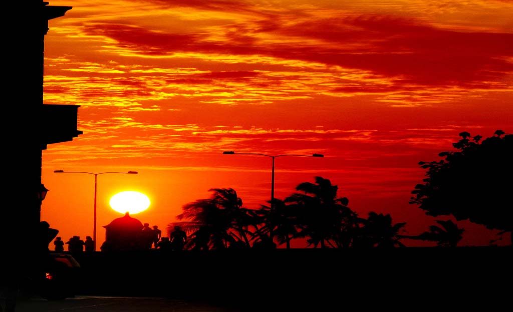 Coucher de soleil rouge orangé sur une rue de Carthagène avec palmiers et lampadaires en silhouette, Colombie