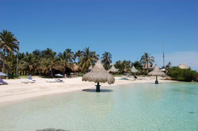 Parasols en paille sur pilotis dans l'eau turquoise, plage bordée de palmiers, île de Múcura, Colombie
