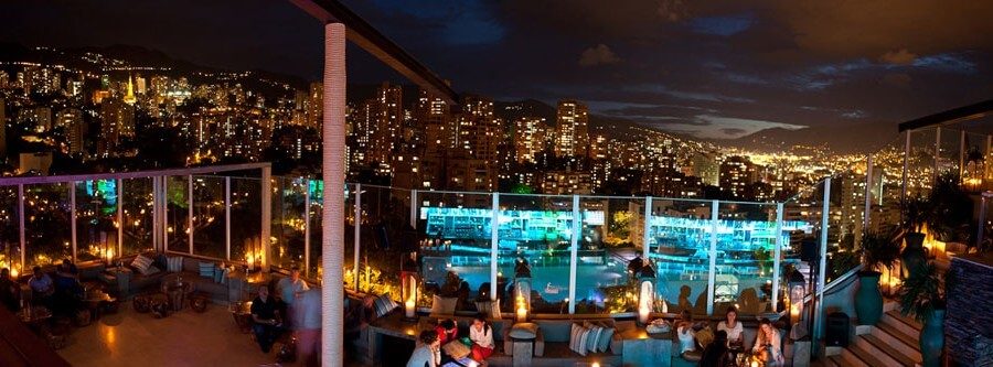 Vue nocturne d'un rooftop bar avec piscine surplombant la ville illuminée de Medellín, Colombie