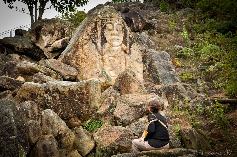 Visiteuse observant un visage précolombien gravé sur un rocher parmi des pierres à San Agustín, Colombie