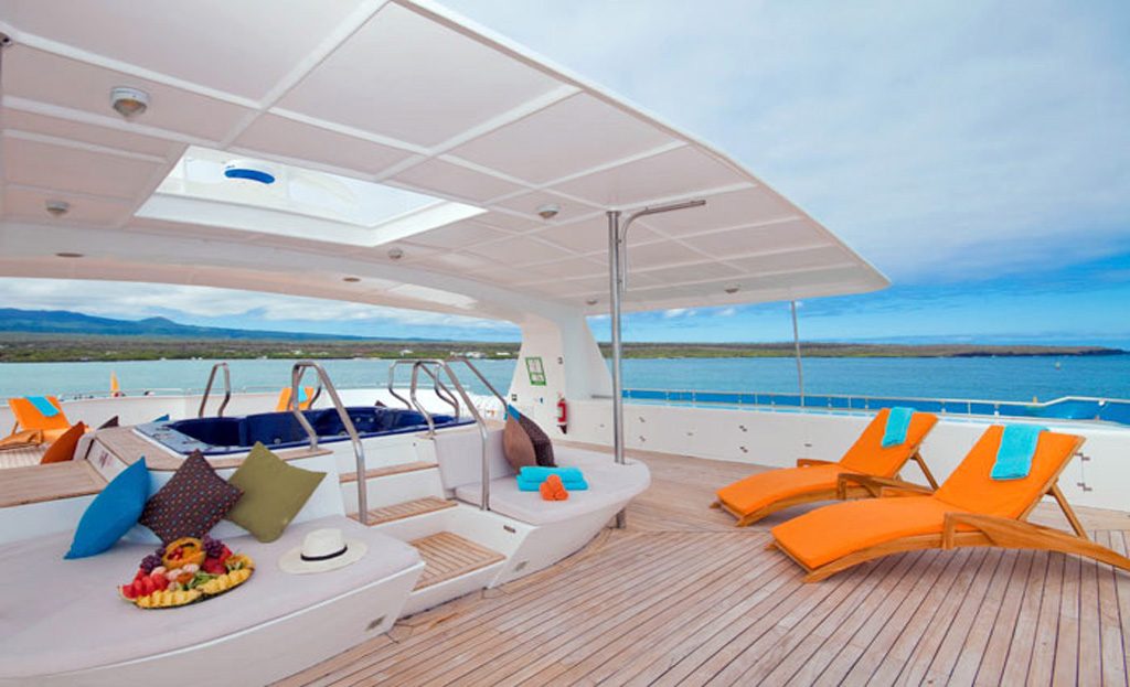 Pont supérieur d'un bateau de croisière avec transats, jacuzzi et vue sur la côte des Galapagos