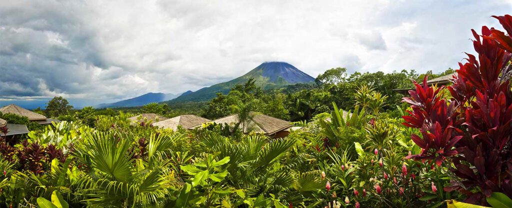 Volcan Arenal au Costa Rica vu depuis un lodge, toits en bois et végétation tropicale luxuriante