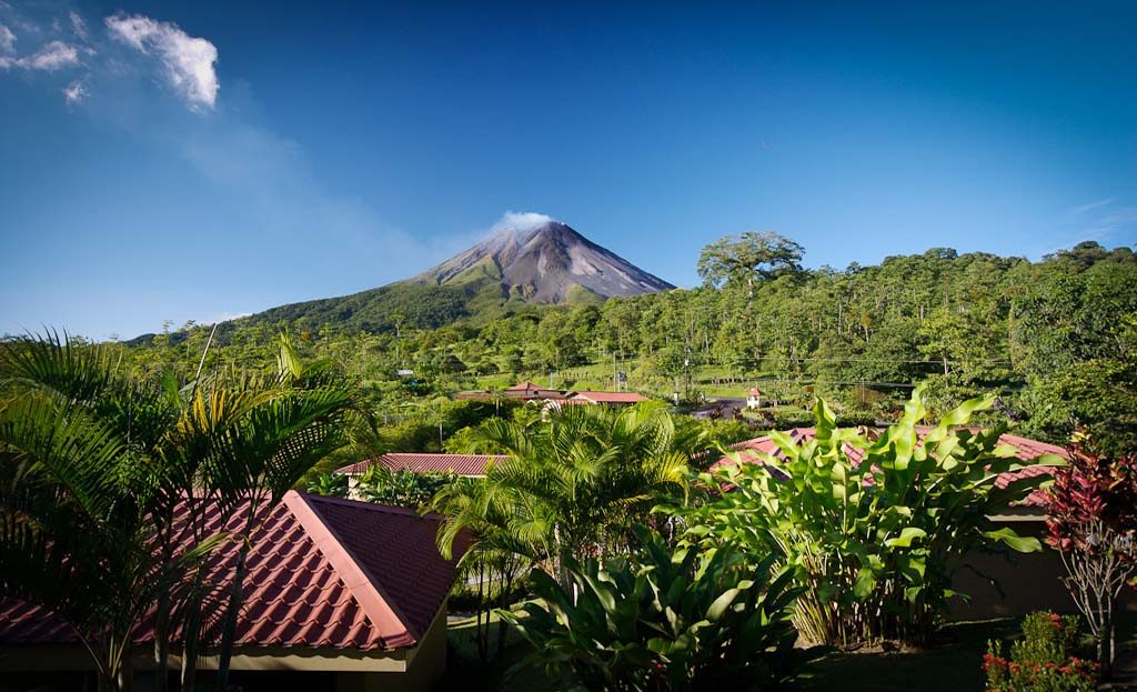 Volcan Arenal fumant vu depuis un lodge avec toits rouges et palmiers, Costa Rica
