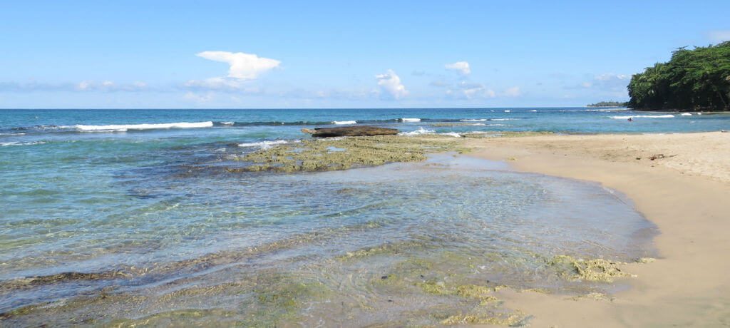 Plage caraïbe du Costa Rica avec eau turquoise, rochers et forêt tropicale en arrière-plan
