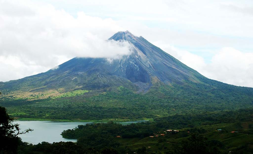 Cône du volcan Arenal avec nuages au sommet, lac et forêt tropicale au premier plan, Costa Rica