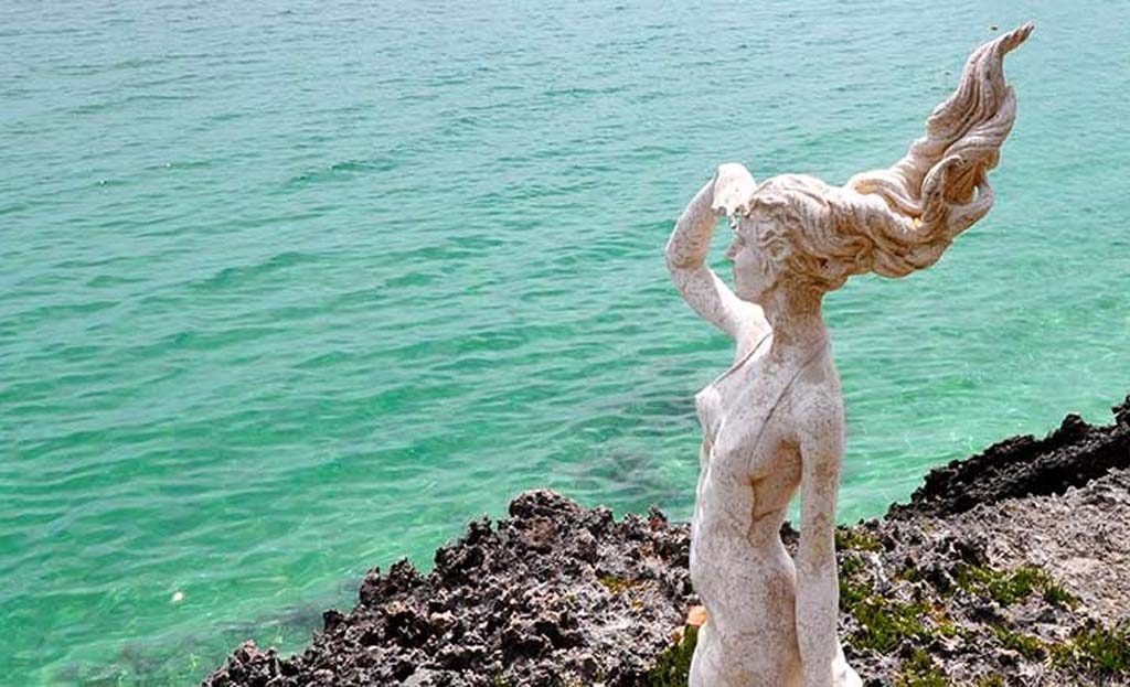 Statue de femme aux cheveux flottants sur rochers face aux eaux turquoise des cayos cubains