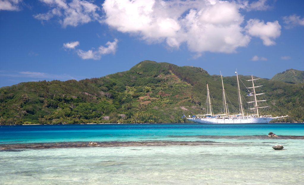 Voilier trois-mâts ancré près d'une île montagneuse verdoyante et lagon turquoise