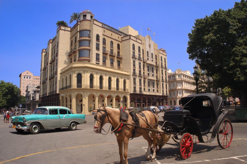 Calèche à cheval et voiture américaine ancienne devant un grand hôtel à La Havane