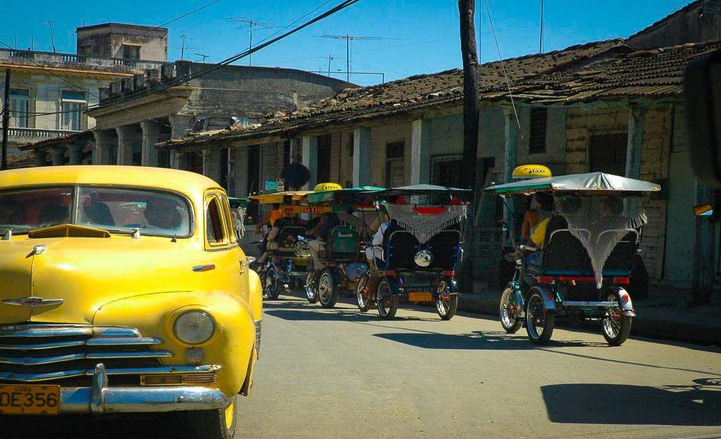 Voiture américaine jaune ancienne et plusieurs vélos-taxis dans une rue de La Havane, Cuba