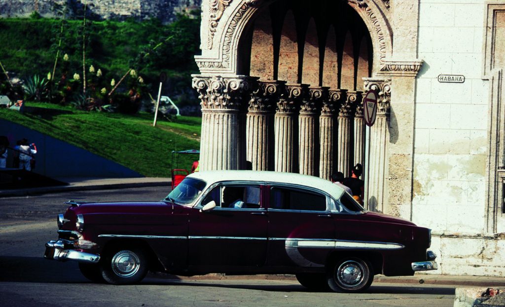Voiture américaine ancienne bordeaux et blanche garée devant un monument à colonnes à La Havane